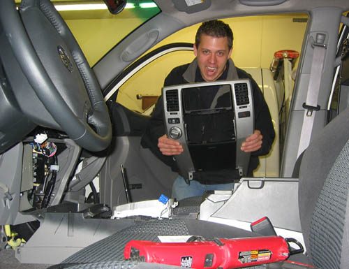 A young Chris Nelson grinning while installing a dash kit inside a truck, tools spread across the seats.